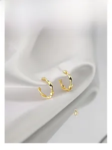 Detailed view of gold Mobius twist hoop earrings on a silky white fabric background