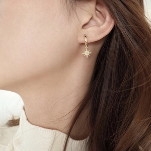 Detail of gold star pendant earrings with micro-pave crystals on a female model