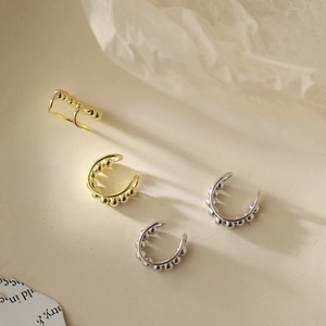 Dettaglio macro di ear cuff a sfere color oro e argento su uno sfondo minimalista