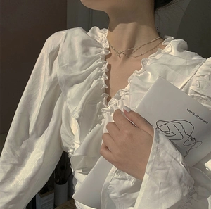Detail of multi-layer silver necklace on model with ruffled white silk shirt