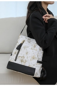Detail of white nylon backpack featuring golden butterfly prints and black leather trim