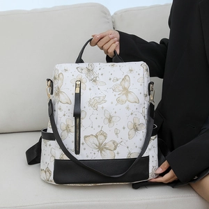 Detail of white nylon backpack featuring golden butterfly prints and black leather trim