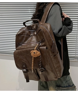 Close-up of vintage brown leather backpack texture with multi-zipper and bear charm