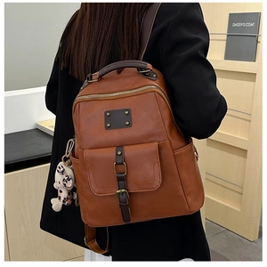 Detail of vintage brown leather backpack with litchi texture and floral bear charm