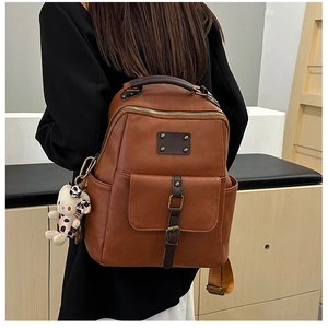 Detail of vintage brown leather backpack showing magnetic front flap and plush cat charm