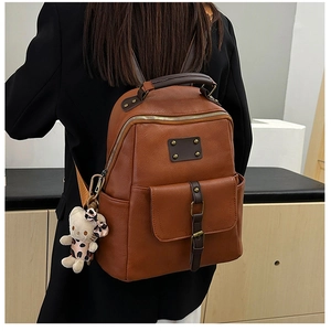 Detail of dark brown leather backpack with front pocket and cute bear plush charm