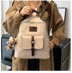 Detail of a beige faux leather backpack with brown trim and plush bear charm on a model