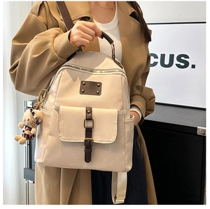 Detail of cream backpack with lychee texture, brown leather straps and bear charm accessory