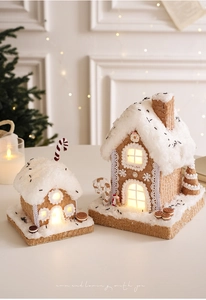 Close-up of lighted gingerbread house ornament with snow roof and candy decorations