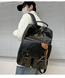 Detail of black textured leather backpack featuring silver zippers and a cute bear charm