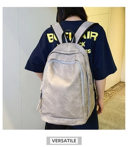 Rear view of a light grey textured backpack with multi-zipper compartments on a model