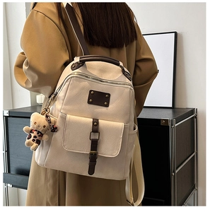 Detail of vintage cream textured faux leather backpack with brown buckle and bear charm
