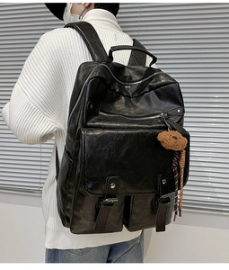Detail of black faux leather backpack featuring dual buckles and brown bear pendant accessory