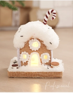Close-up of lighted gingerbread house ornament with snowy roof and warm LED glow