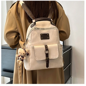 Detailed view of a minimalist beige backpack with brown leather straps and plush bear charm