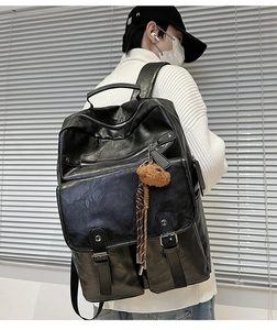 Detail of black faux leather backpack featuring dual buckles and brown plush bear charm