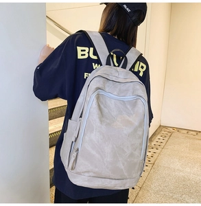Detailed back view of a minimalist light gray backpack worn by a model in casual style