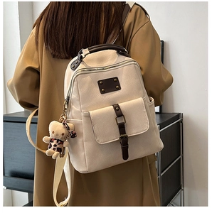 Detail of cream pebbled leather backpack with brown handles and a teddy bear charm