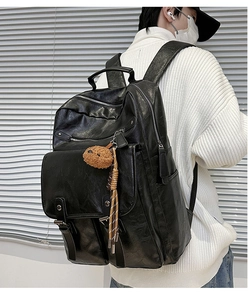 Detail of a black PU leather laptop backpack featuring a brown plush bear charm and side pockets