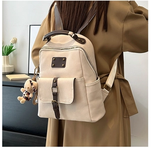 Detail of minimalist beige backpack with dark brown straps and leopard bear plush charm