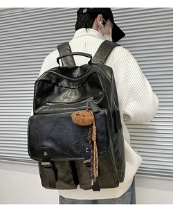 Detail of black faux leather backpack featuring a cute brown plush bear charm accessory