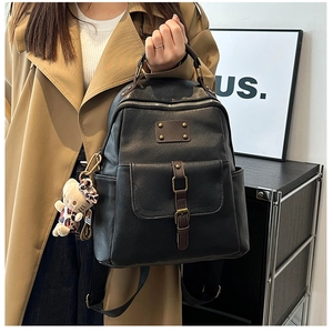 Detail of a black PU leather backpack with brown straps and a cute leopard bear pendant