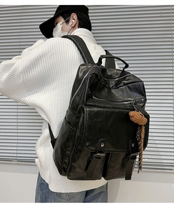 Detail of black leather laptop backpack with buckle straps and plush bear charm