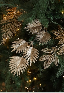 Feuille de fougère dorée scintillante sur sapin de Noël avec fond lumineux chaleureux