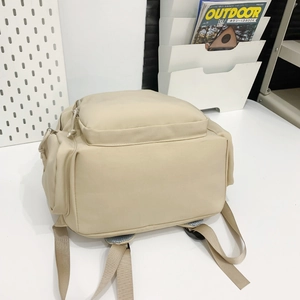 Detail of minimalist nylon school backpack with zip pocket and side compartments in beige