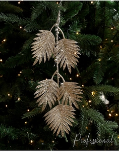 Gros plan d'une feuille de palmier artificielle dorée sur un sapin de Noël illuminé