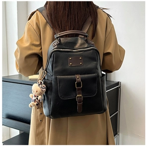 Detail view of vintage black leather backpack with brown straps and plush cat charm