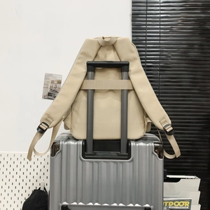 Detail view of beige nylon backpack with suitcase strap attached to silver luggage handle