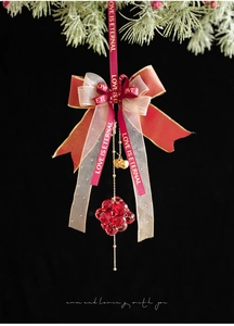 Close-up of a Christmas bow ornament with red crystals and small gold bells on pine