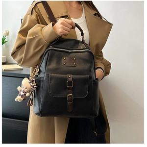 Detail of black faux leather backpack with brown strap accent and cute bear charm pendant
