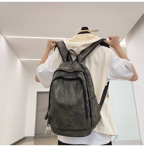 Dark grey-green backpack shown on model in a minimalist modern indoor setting
