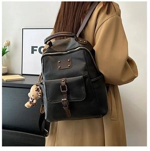 Detail of a vintage black leather backpack with brown handles and a stylish side charm