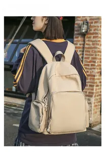 Outdoor shot of cream nylon backpack featuring multiple zip pockets and wide shoulder straps