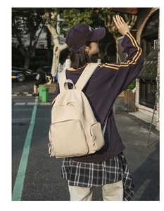 Outdoor side view of a minimalist cream nylon backpack with functional pockets on a model