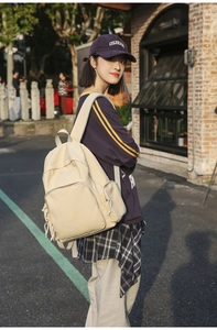 Detail view of a beige minimalist nylon backpack with side pockets on a person