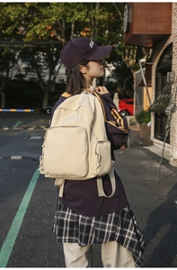 Outdoor street view of a beige nylon backpack with large front pocket and adjustable straps