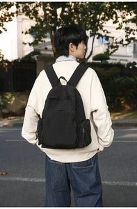 Outdoor shot of the black minimalist backpack showing wide straps and side zip pockets