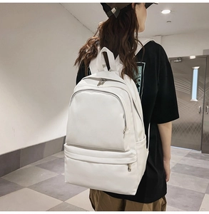 Rear view of model wearing a large white canvas backpack in a minimalist indoor setting