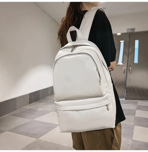 Side view of white faux leather backpack shown on a model in a modern urban setting