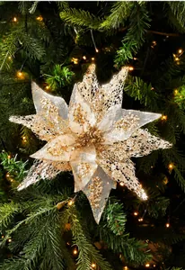 Detail of glitter champagne mesh poinsettia flower on a lit Christmas tree branch