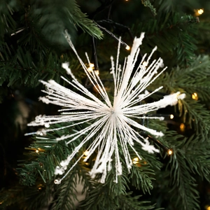 Sparkling white snowflake ornament with glitter finish on a green Christmas tree