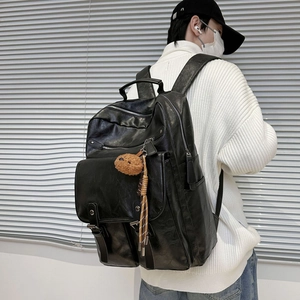 Black matte leather backpack with plush charm, showing spacious design on male model