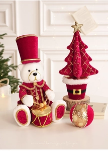 Orsetto natalizio di peluche in divisa di velluto accanto a mini albero e decorazione