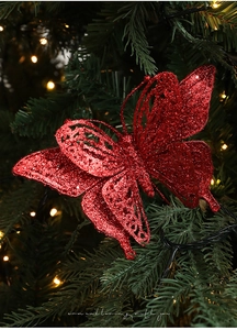 Close-up of glittery red butterfly ornament on green Christmas tree branch