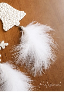 Detail of white pearl beaded Christmas ornament featuring soft feather tassels on wood