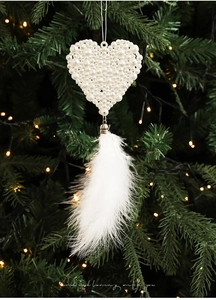 Detail of white faux pearl heart ornament with feather tassel hanging on a Christmas tree